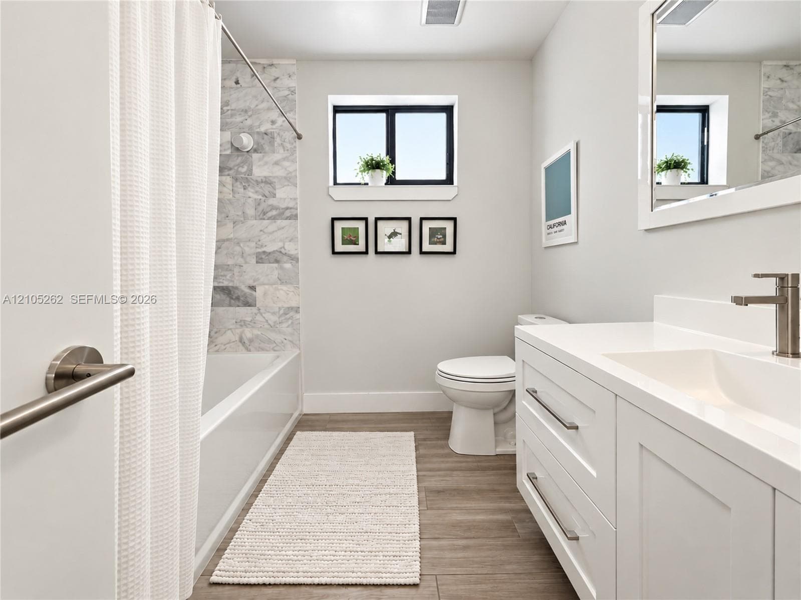Bathtub with tiled surround, wood-finish flooring, white vanity with integrated sink, and brushed nickel fixtures