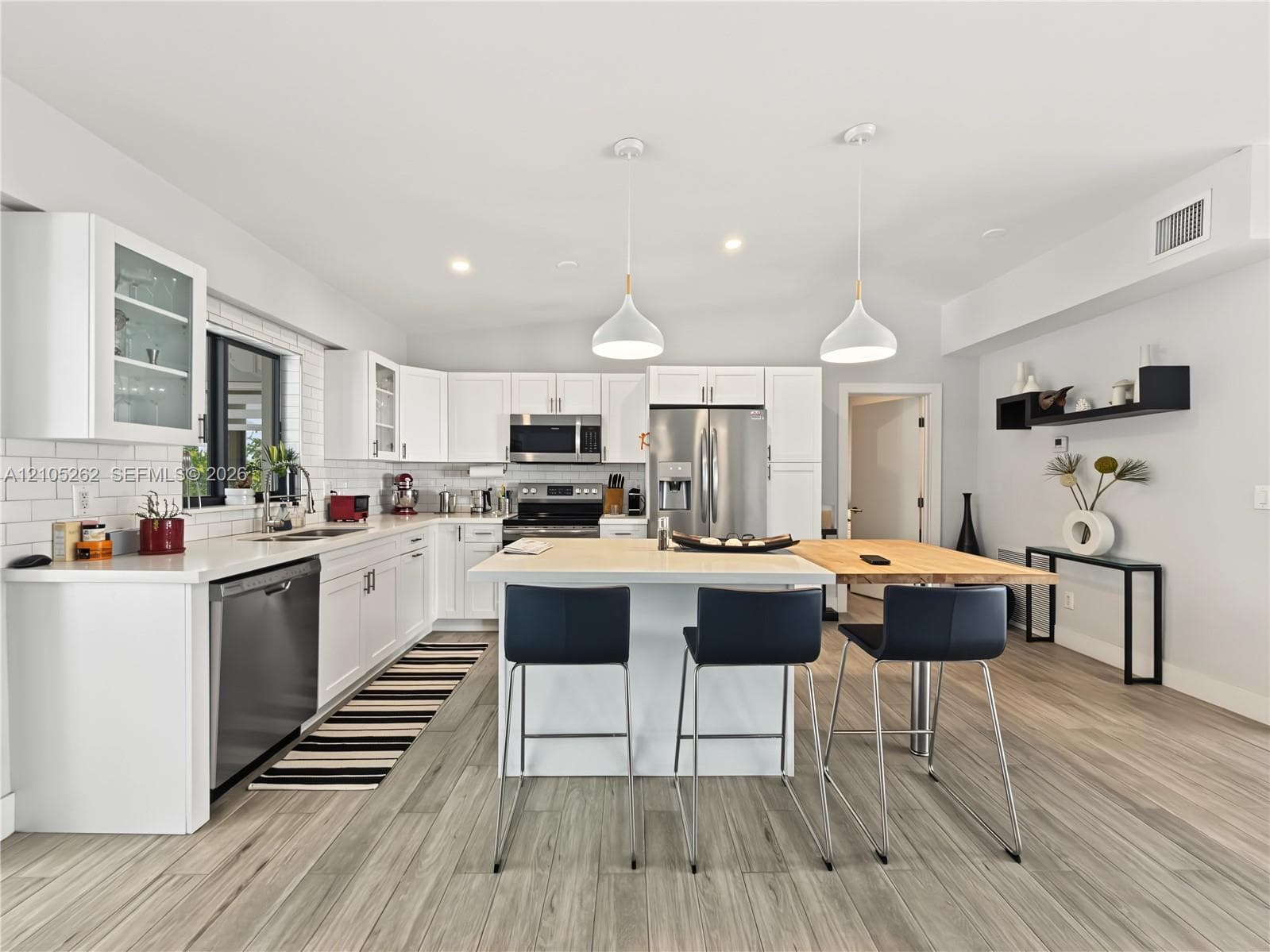 Kitchen featuring white cabinetry, subway tile backsplash, stainless steel appliances, a center island with seating, and wood-finish flooring