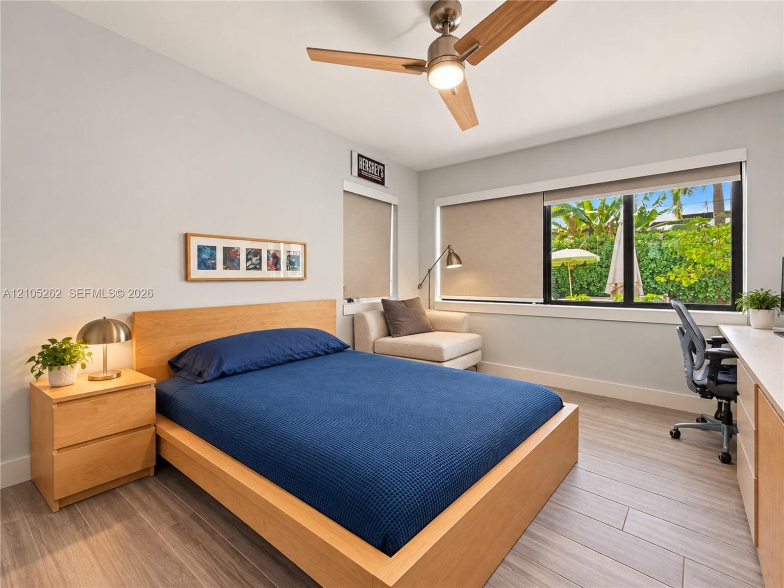 Recessed window with roller shades, wood-finish flooring, ceiling fan with integrated lighting, built-in desk, and light-toned walls