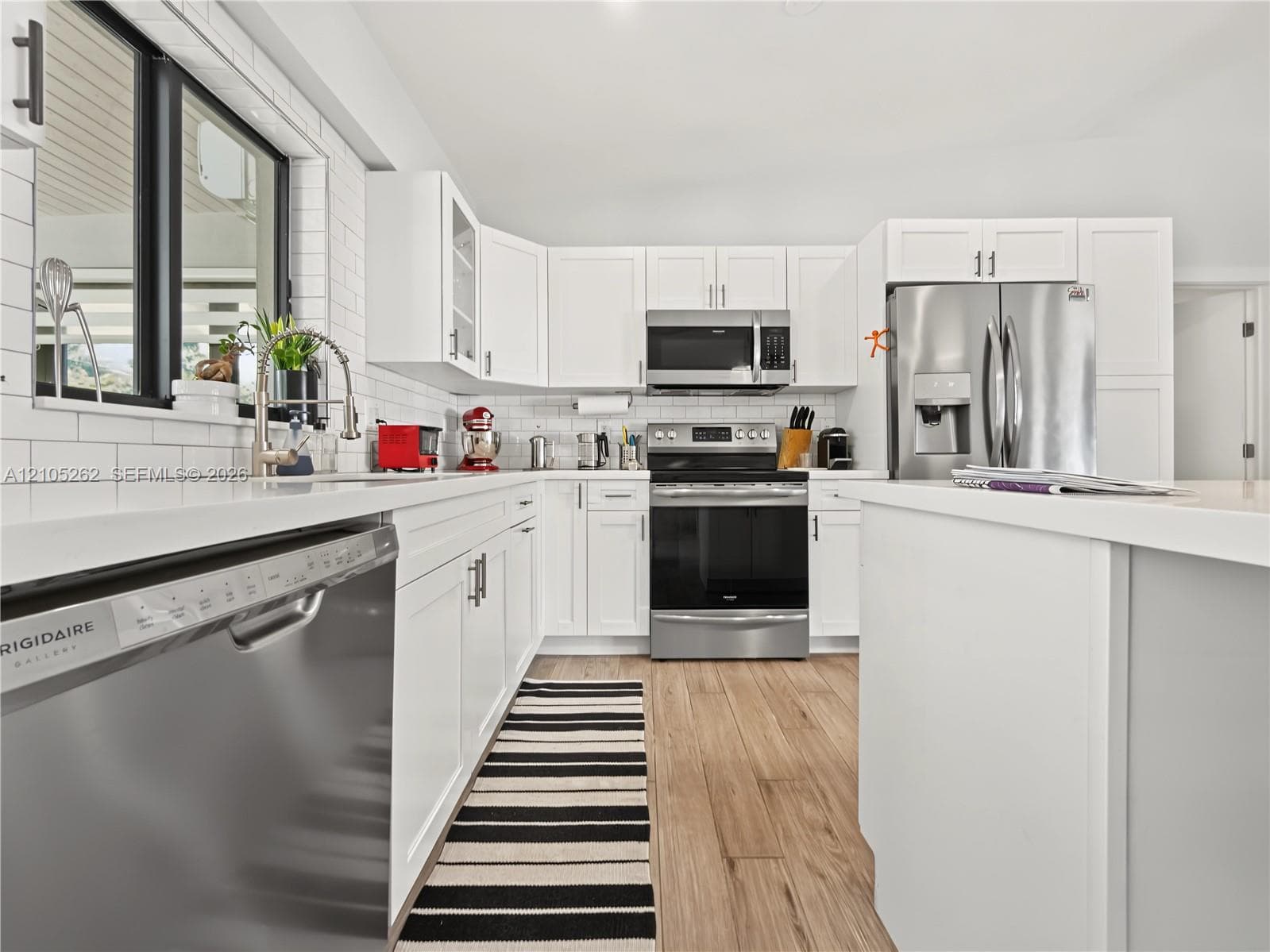 Modern kitchen featuring white cabinetry, stainless steel appliances, light-toned countertops, subway tile backsplash, and wood-finish flooring