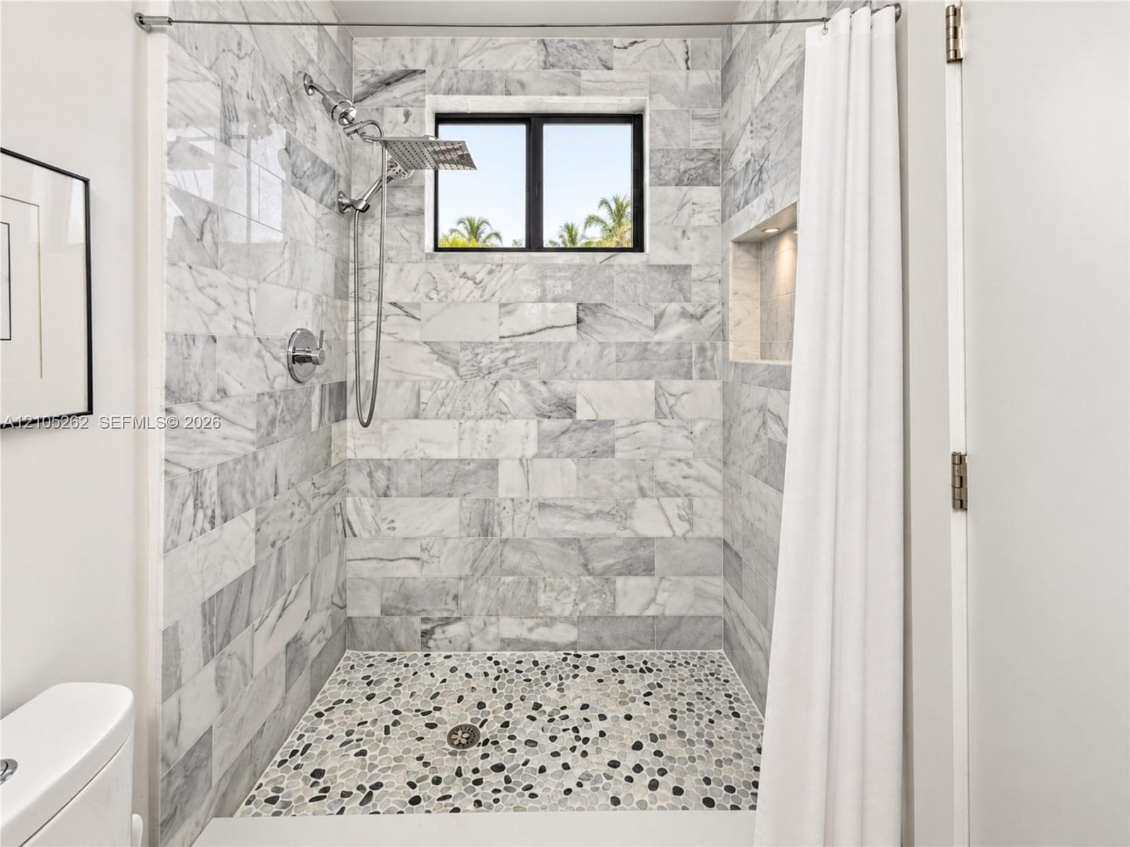 Tiled shower with a rainfall showerhead, handheld sprayer, built-in recessed niche, and pebble-style floor