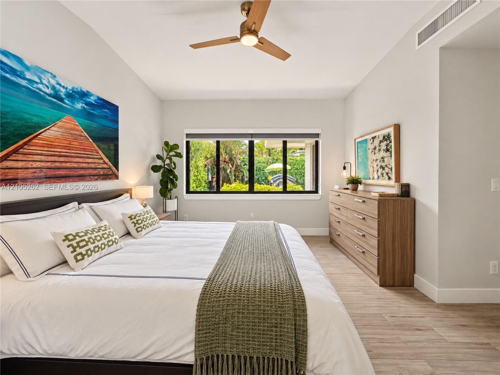 Vaulted ceiling, wood-finish flooring, ceiling fan, wide window with exterior views, and a built-in air conditioning vent