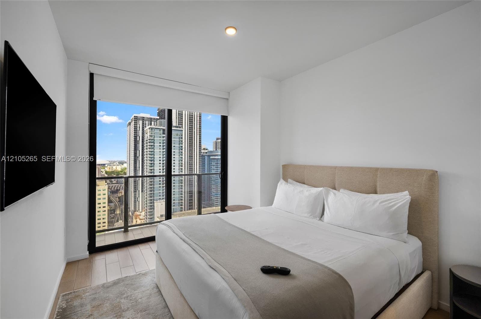 Floor-to-ceiling windows featuring urban skyline scenery, integrated glass-panel balcony, and wood-finish flooring