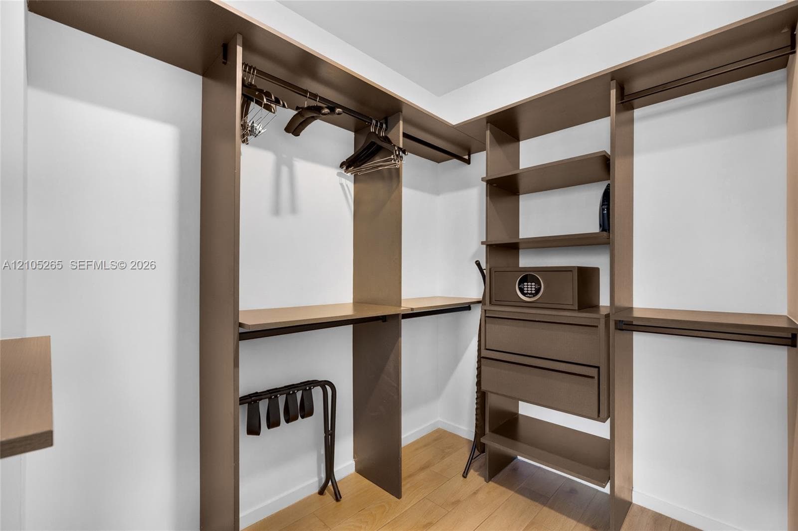Walk-in closet featuring custom laminate shelving, integrated hanging rods, built-in drawer storage, and wood-finish flooring