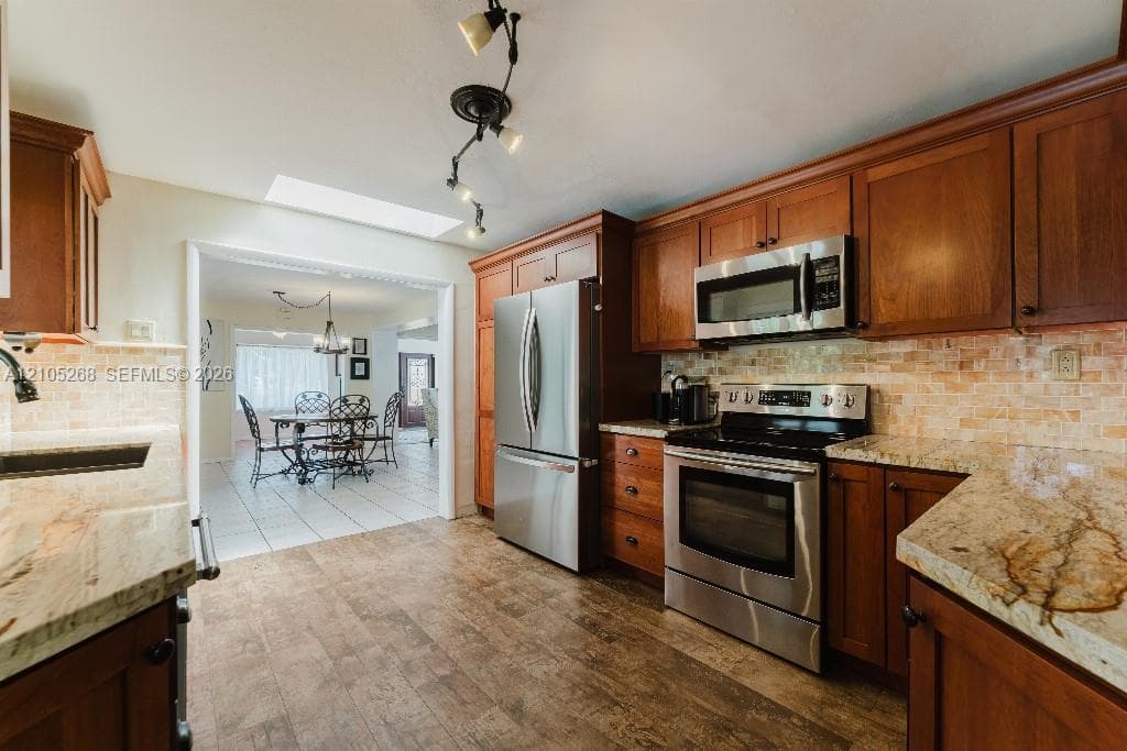 Wood-finish flooring with a skylight, full suite of stainless steel appliances, and stone countertops