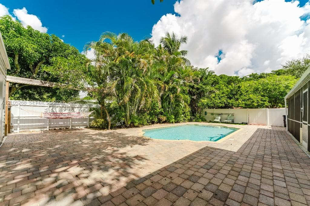 Outdoor swimming pool with a paver patio and mature tropical landscaping
