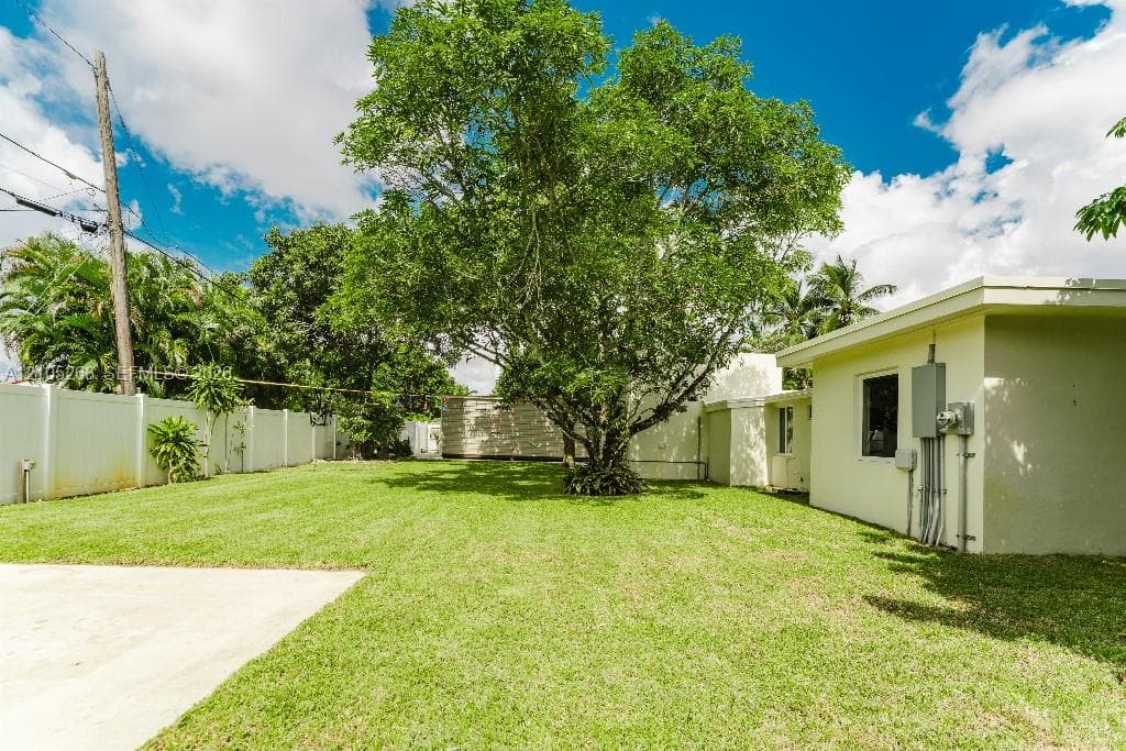 Expansive grass lawn with a mature central tree, concrete patio, and perimeter fencing