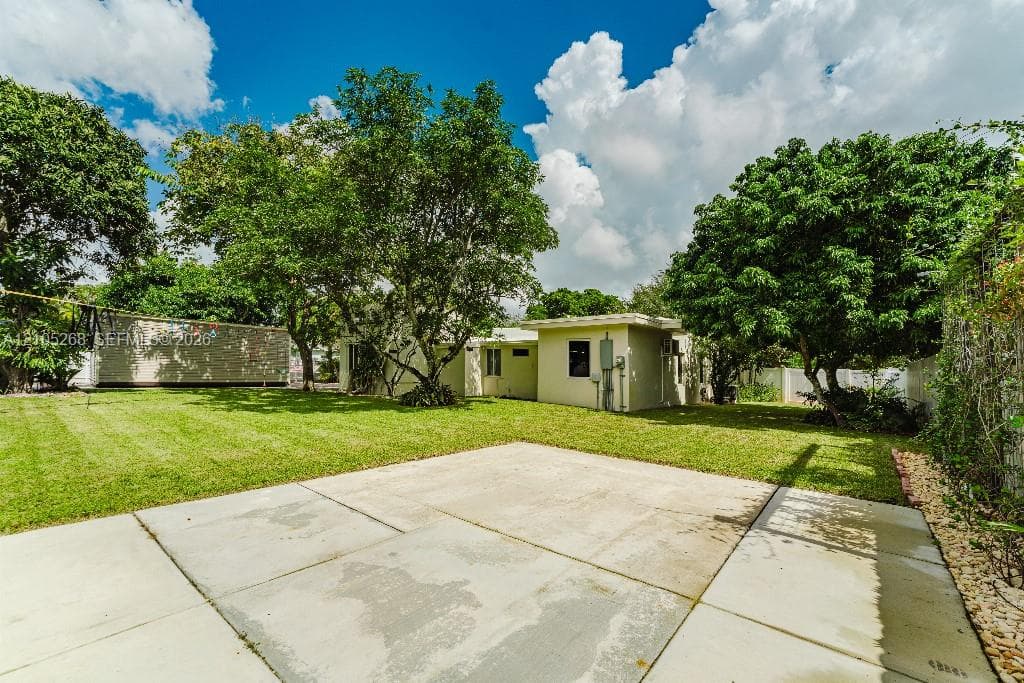 Expansive concrete patio with a lush green lawn and mature trees