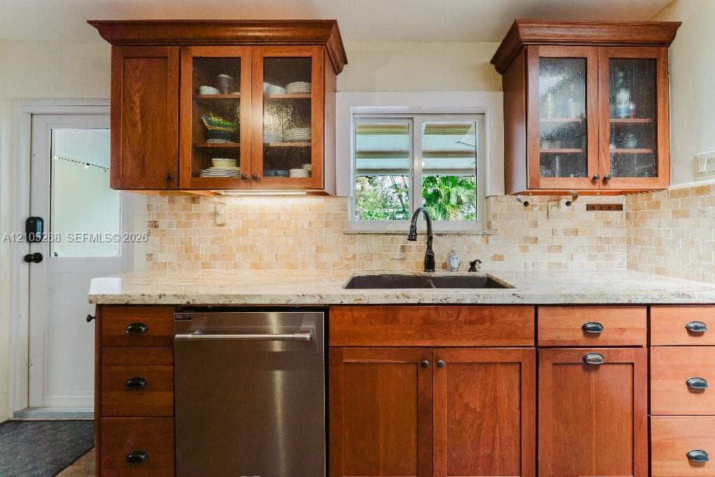 Wood cabinetry with glass-front upper cabinets, stainless steel dishwasher, speckled countertops, and a mosaic tile backsplash