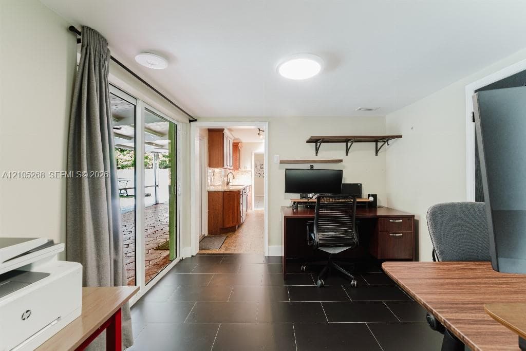 Black tile flooring, sliding glass door, built-in shelving, recessed ceiling lighting, and a doorway opening to a kitchen