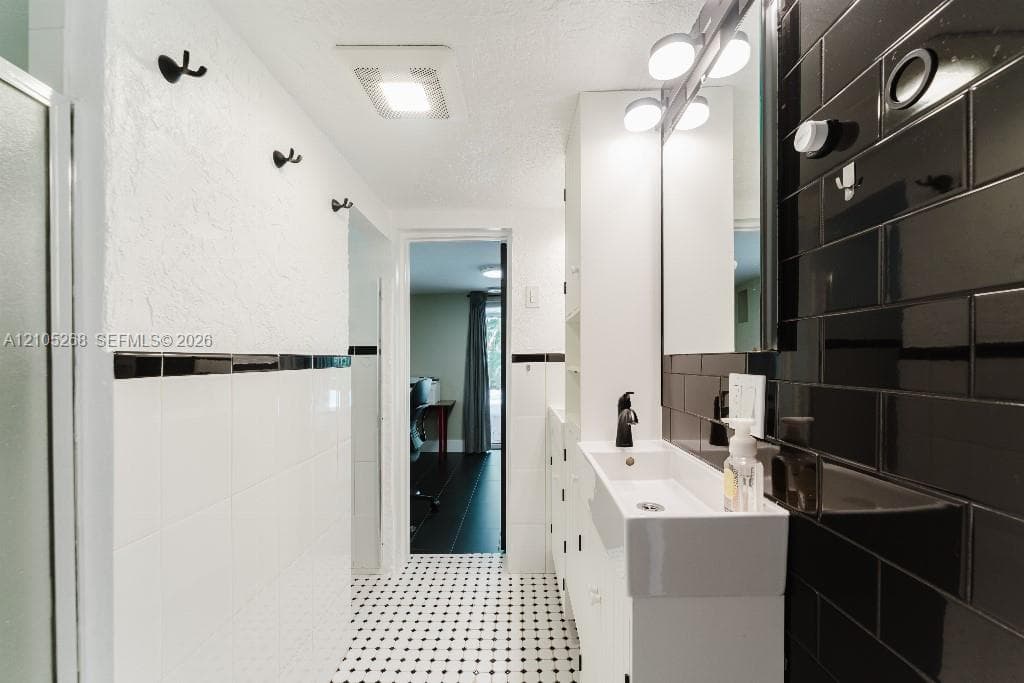 Black and white tile flooring, white subway tile wainscoting, black subway tile accent wall, contemporary vanity with integrated sink, and matte black faucet