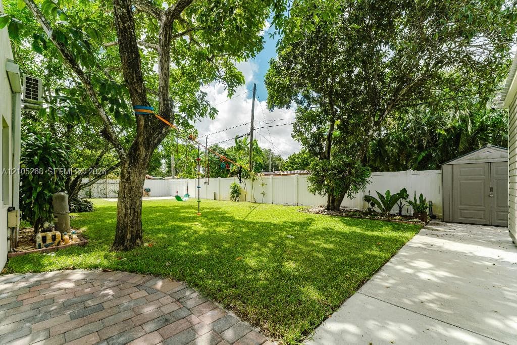 Manicured lawn, mature trees, white privacy fencing, paved patio area, and a storage shed