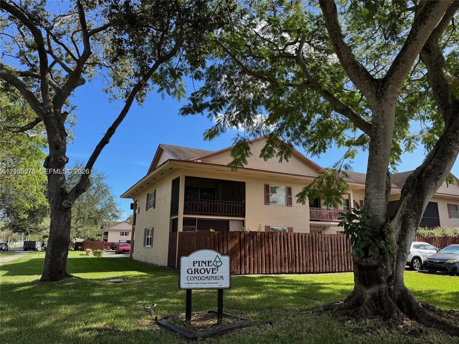 Two-story condominium building featuring a balcony, exterior shutters, and a wood privacy fence