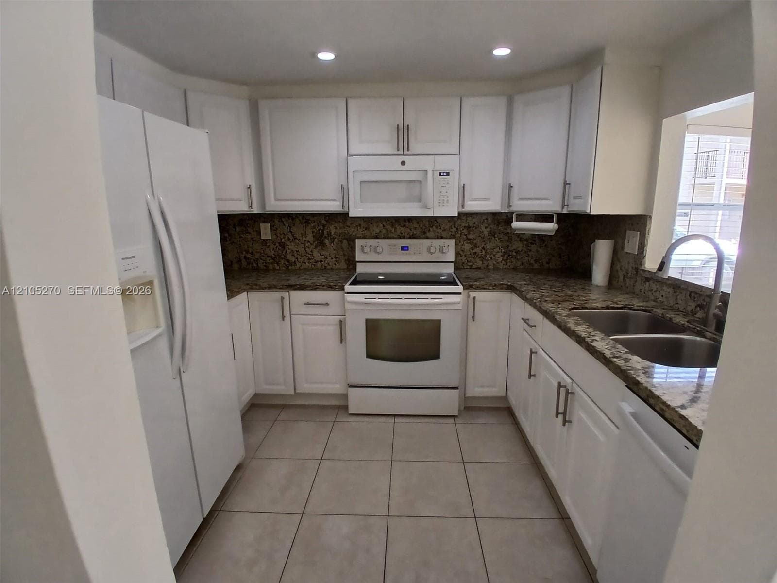 U-shaped kitchen with white cabinetry, stainless steel sink, granite countertops, and tile flooring