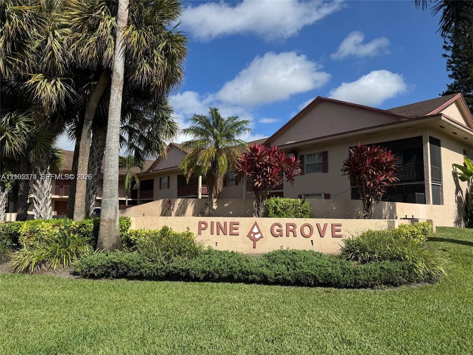 Prominent property signage, mature palm trees, established landscaping, screened outdoor living spaces, and a neutral-toned building exterior