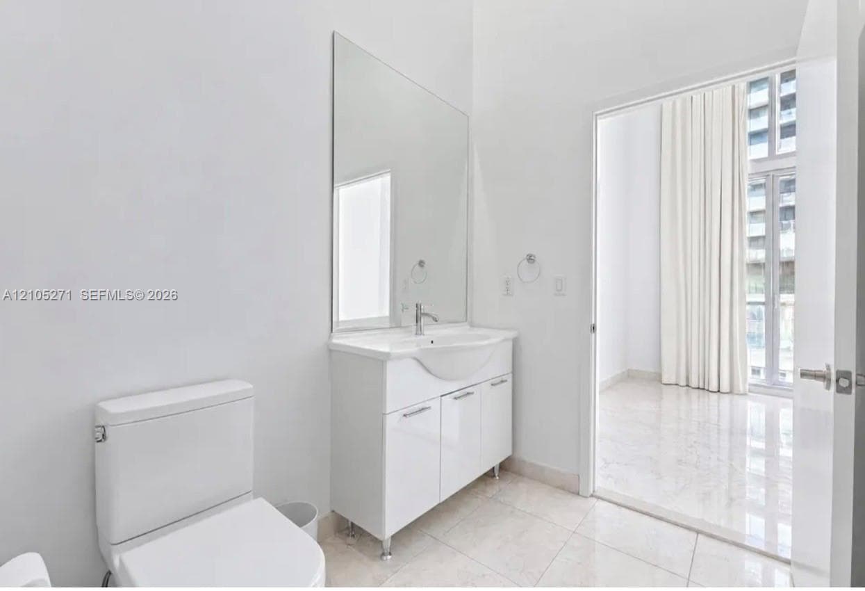 Bathroom featuring a white vanity cabinet with a integrated sink, polished chrome faucet, full-height wall mirror, and large-format tile flooring