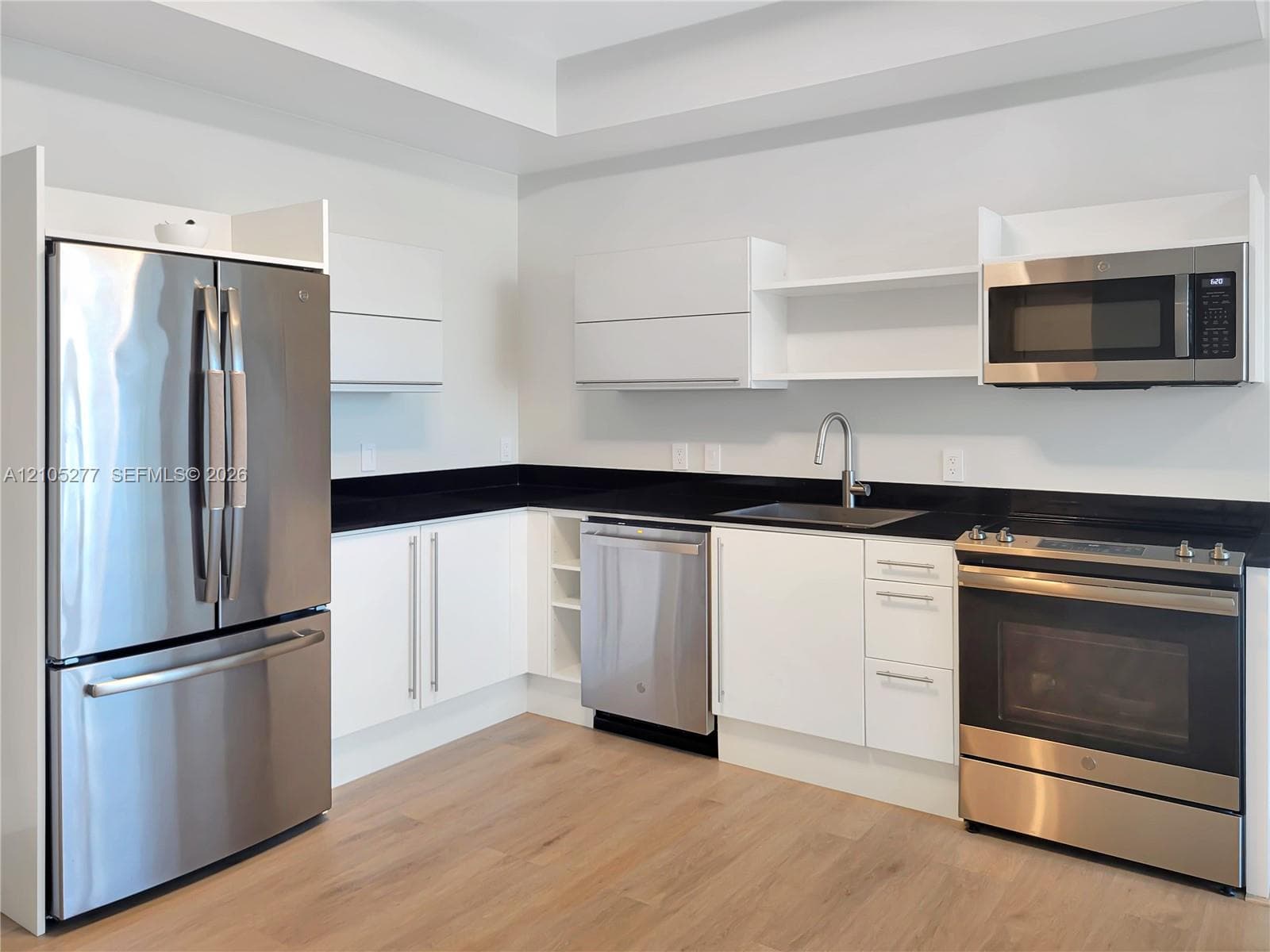 Modern kitchen featuring stainless steel appliances, dark countertops, white cabinetry, a single basin sink, and wood-finish flooring