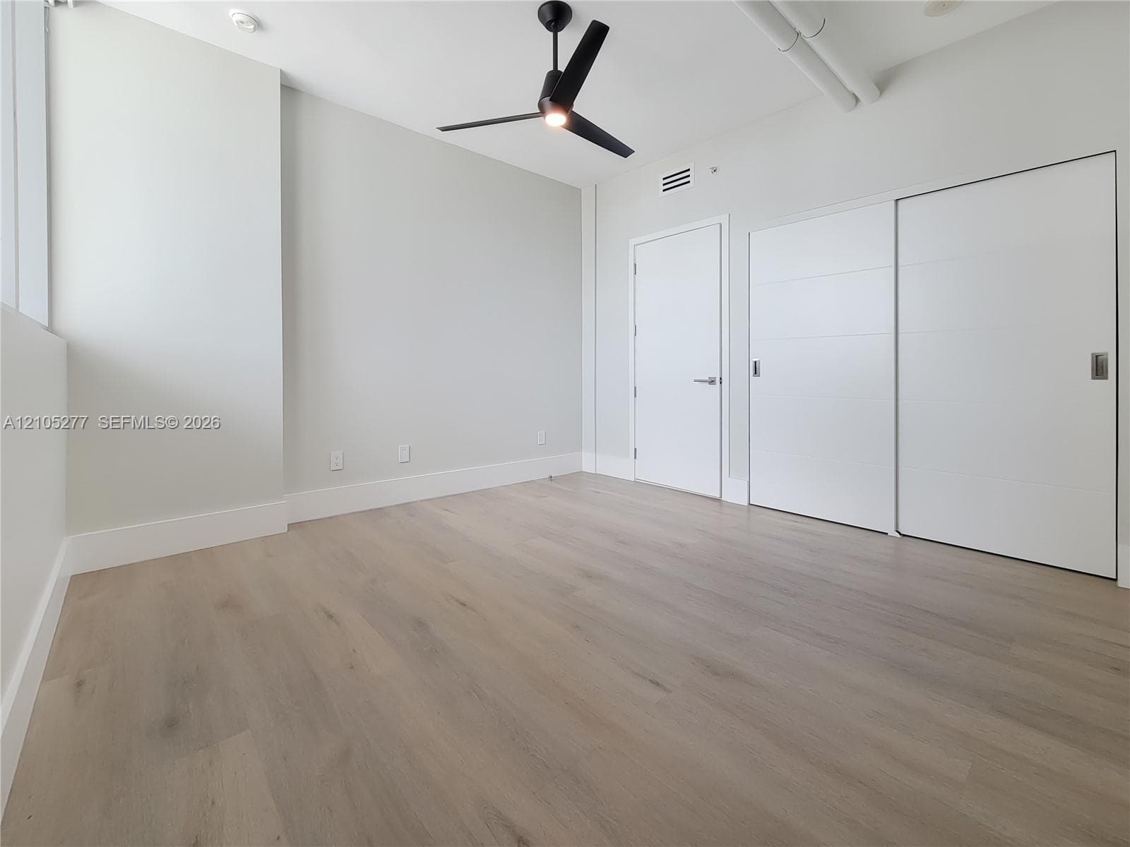 Wood-finish flooring, high ceilings, ceiling fan, white walls, and built-in sliding closet doors