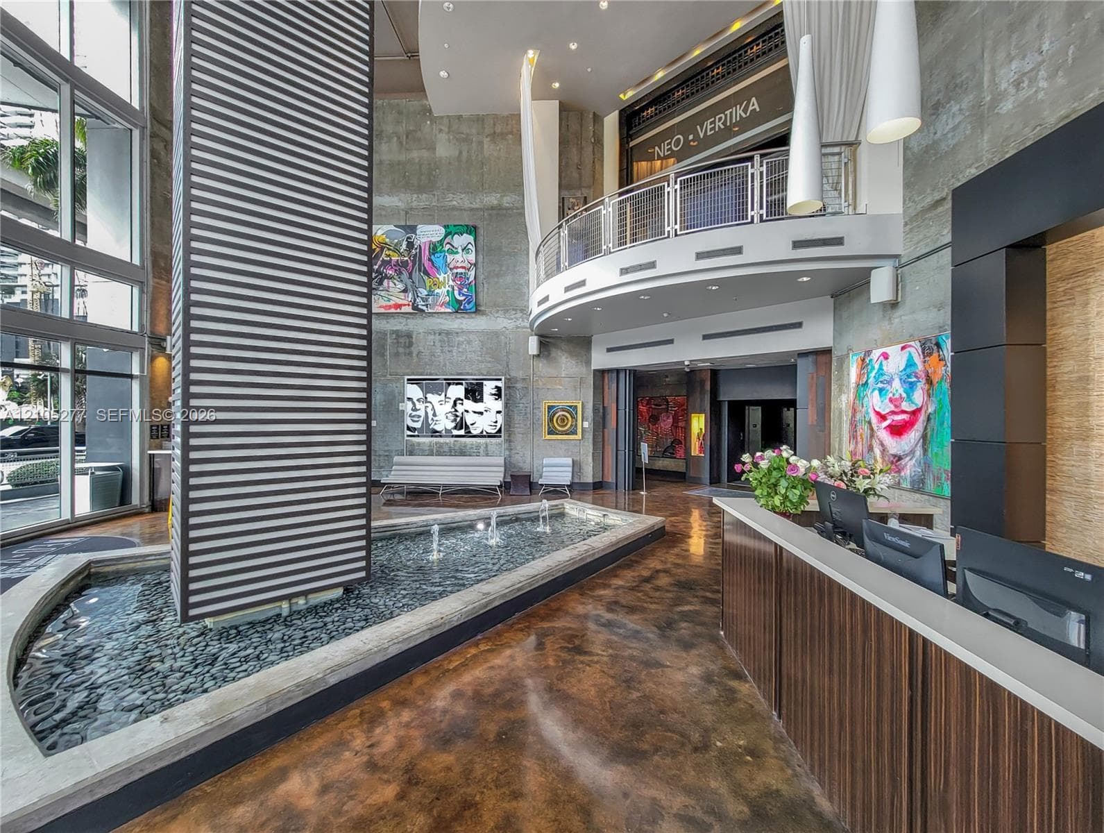 Two-story lobby featuring an indoor water feature, polished concrete flooring, a custom reception desk, and a second-level balcony