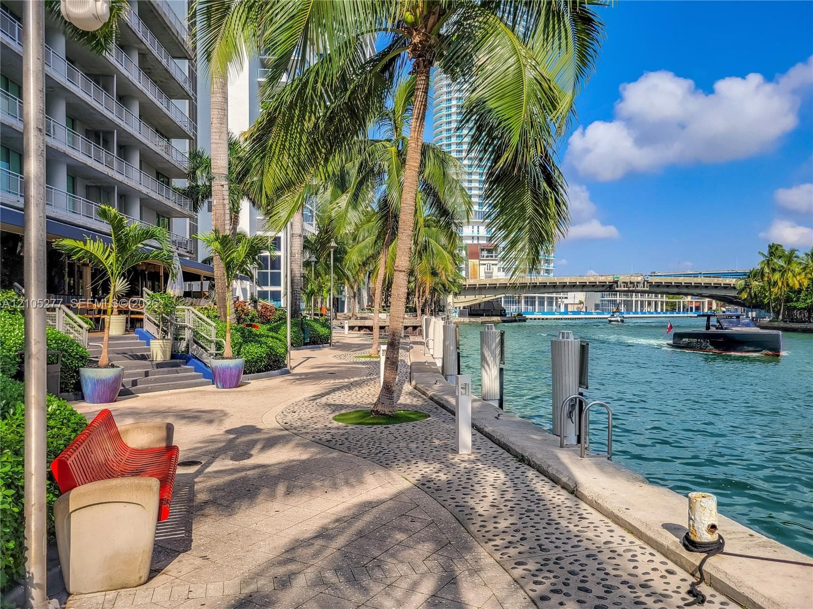 Waterfront promenade with lush landscaping, paved walkways, and a contemporary multi-story building