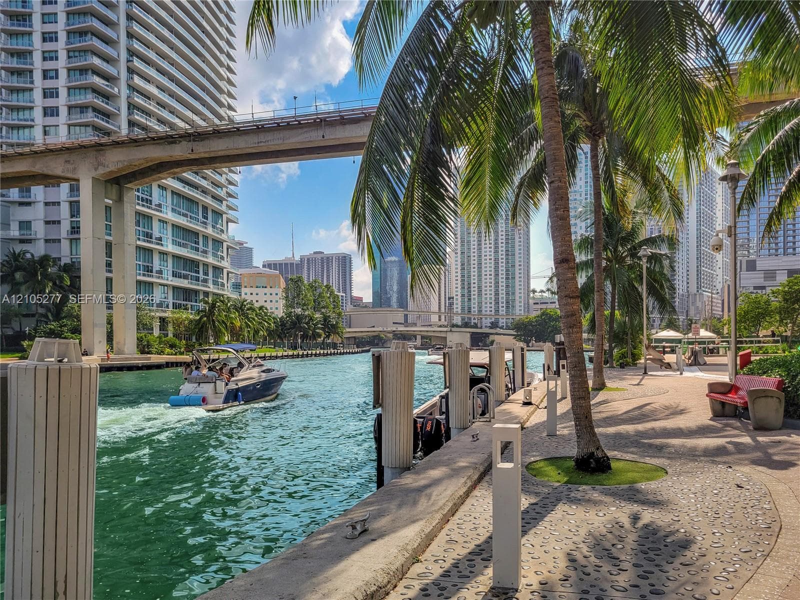 Waterfront promenade featuring a paved walkway, mature palm trees, and modern lighting fixtures