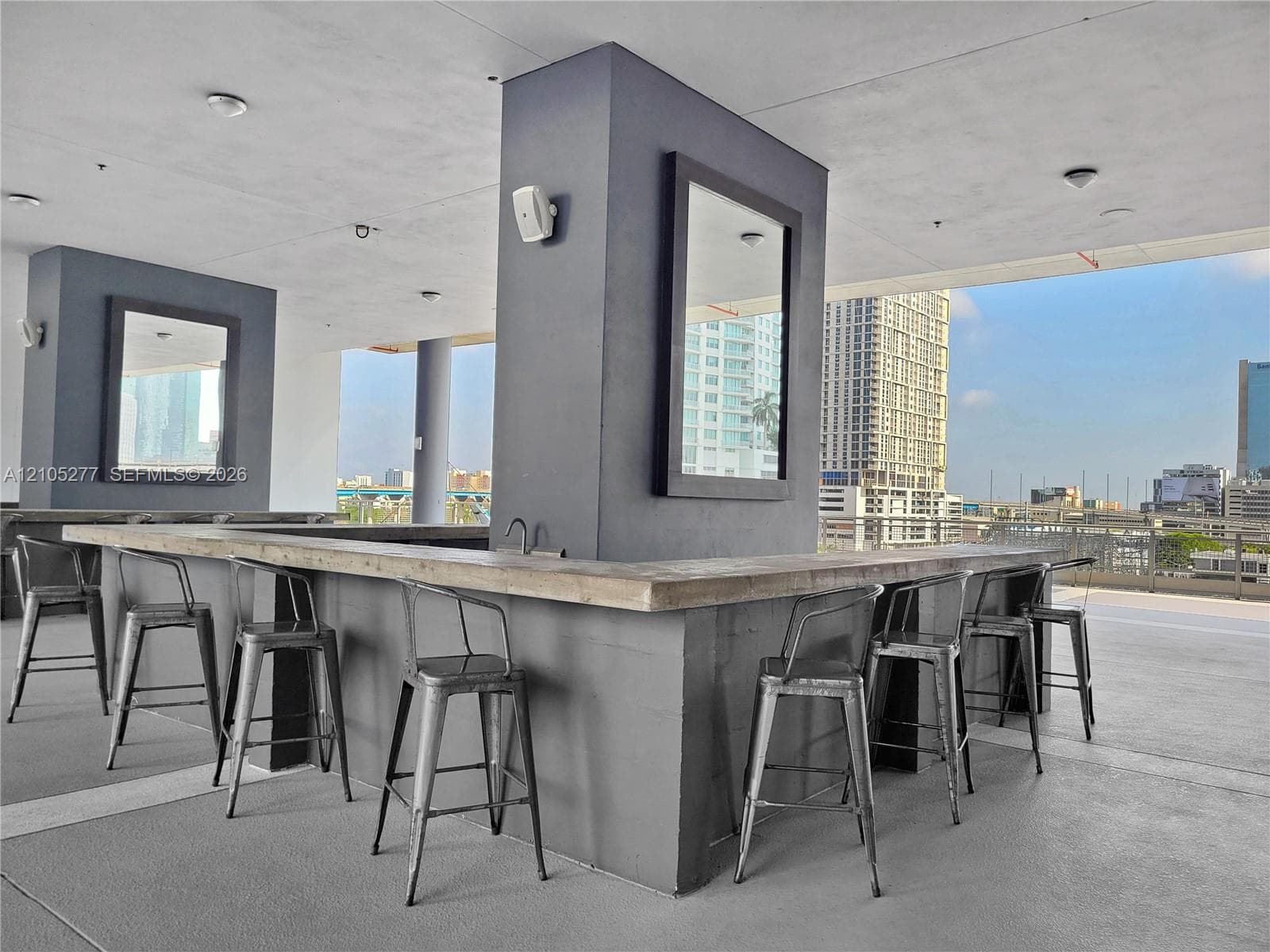 Open-air lounge area with a built-in bar, concrete-finish countertop, and a high-rise urban backdrop