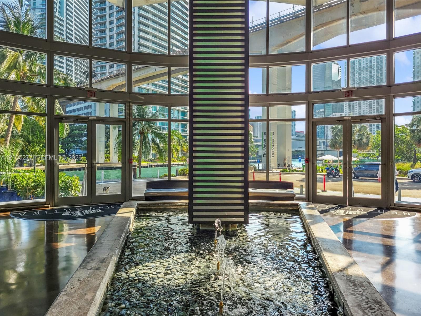 Curved window wall with multiple glass entry points, central water feature with stone base and pebble bed, and polished dark flooring