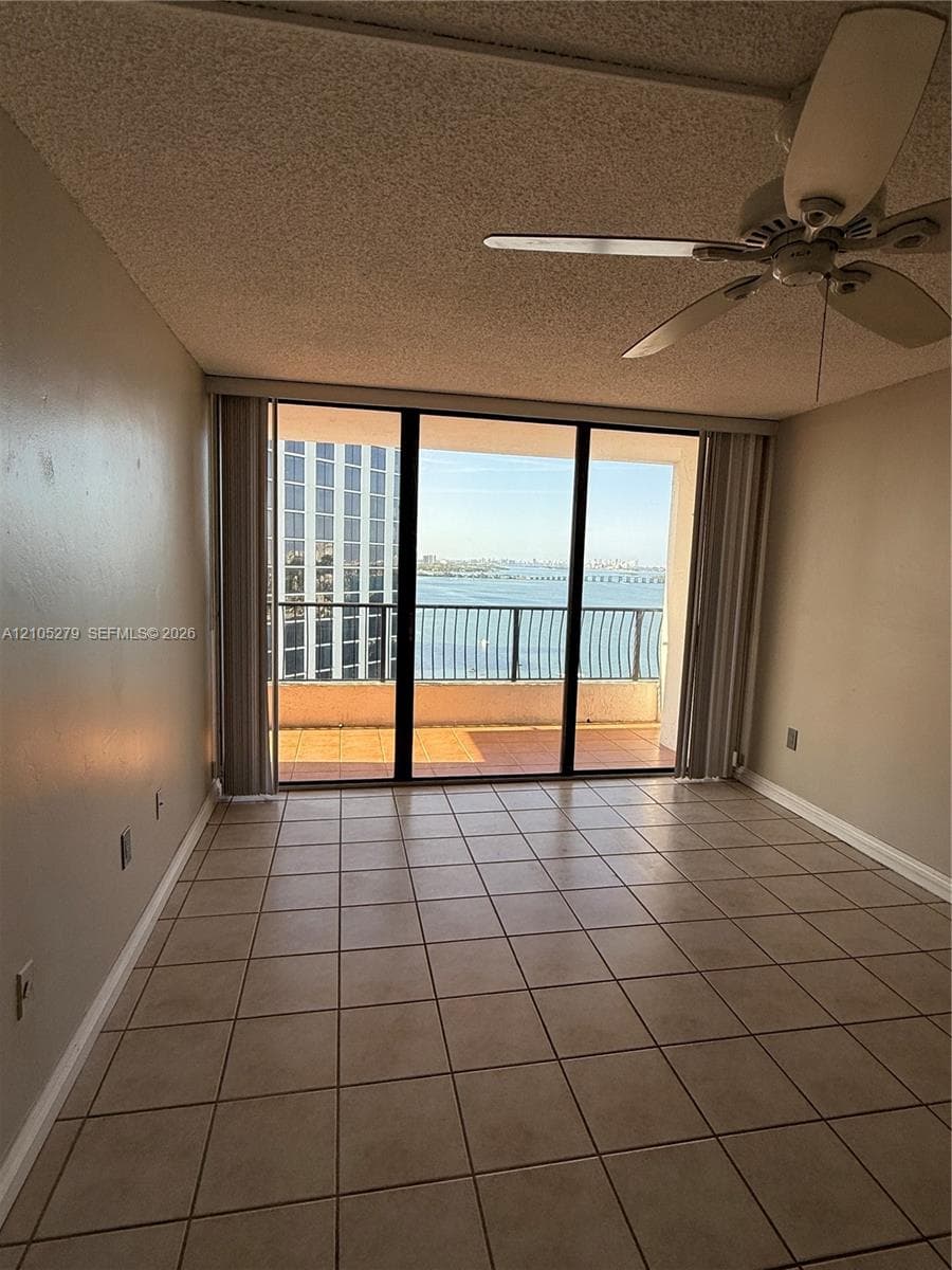 Tile flooring, sliding glass door balcony access, ceiling fan, and city-water backdrop