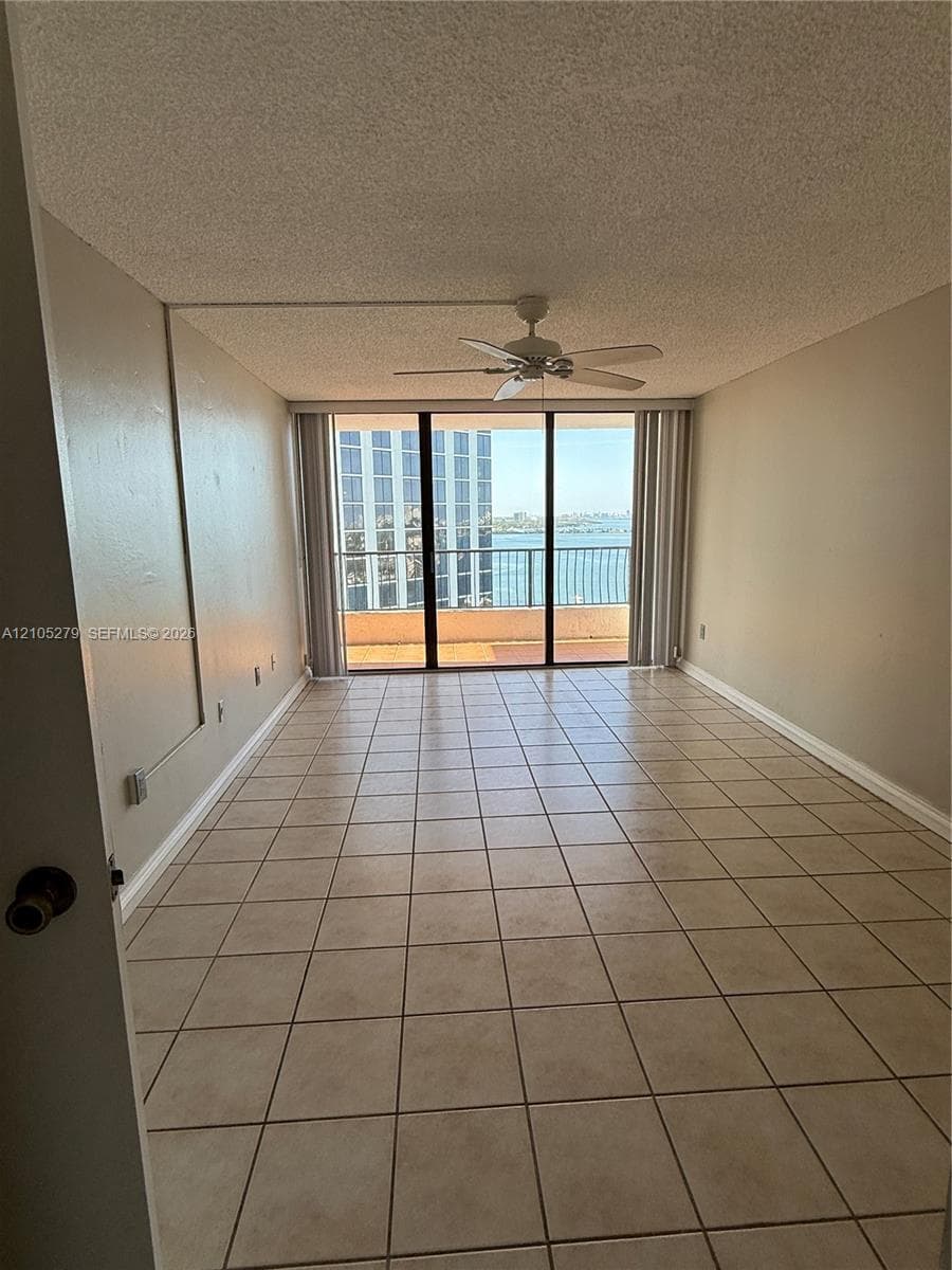 Spacious room featuring neutral-toned tile flooring, direct access to a private balcony, and a ceiling fan