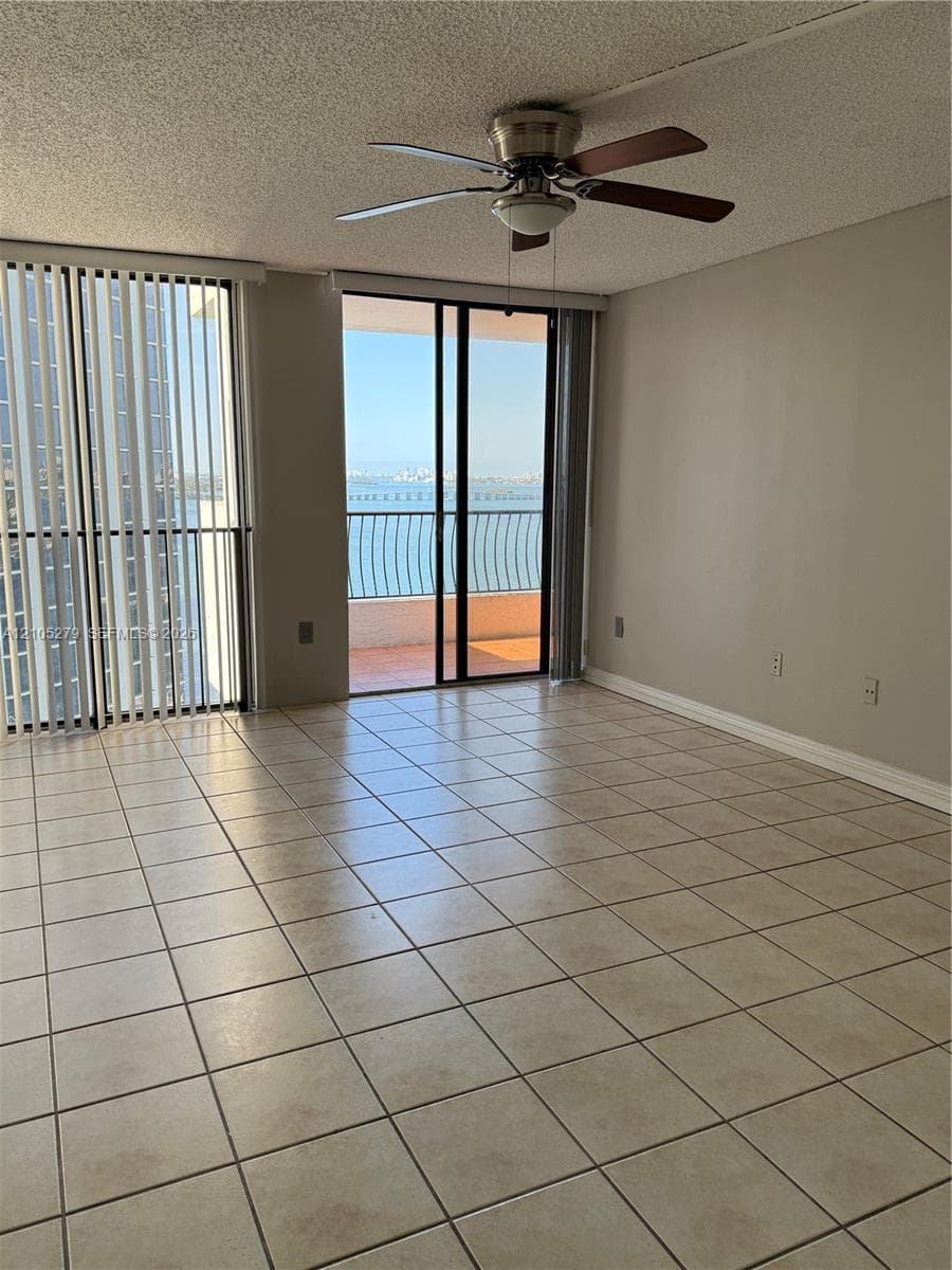 Expansive tiled flooring, direct balcony access, ceiling fan with light fixture, and vertical blinds
