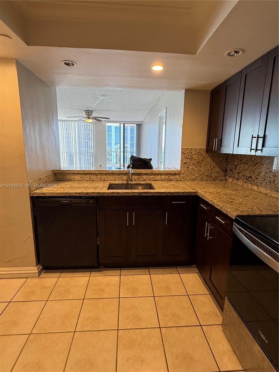 U-shaped kitchen with brown wood-finish cabinetry, speckled countertops, stainless steel sink, and tile flooring