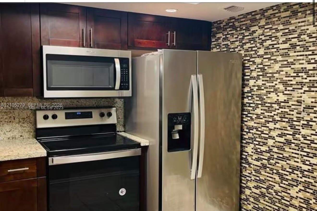 Stainless steel appliances, rich wood-finish cabinetry, patterned mosaic tile backsplash, and speckled countertops