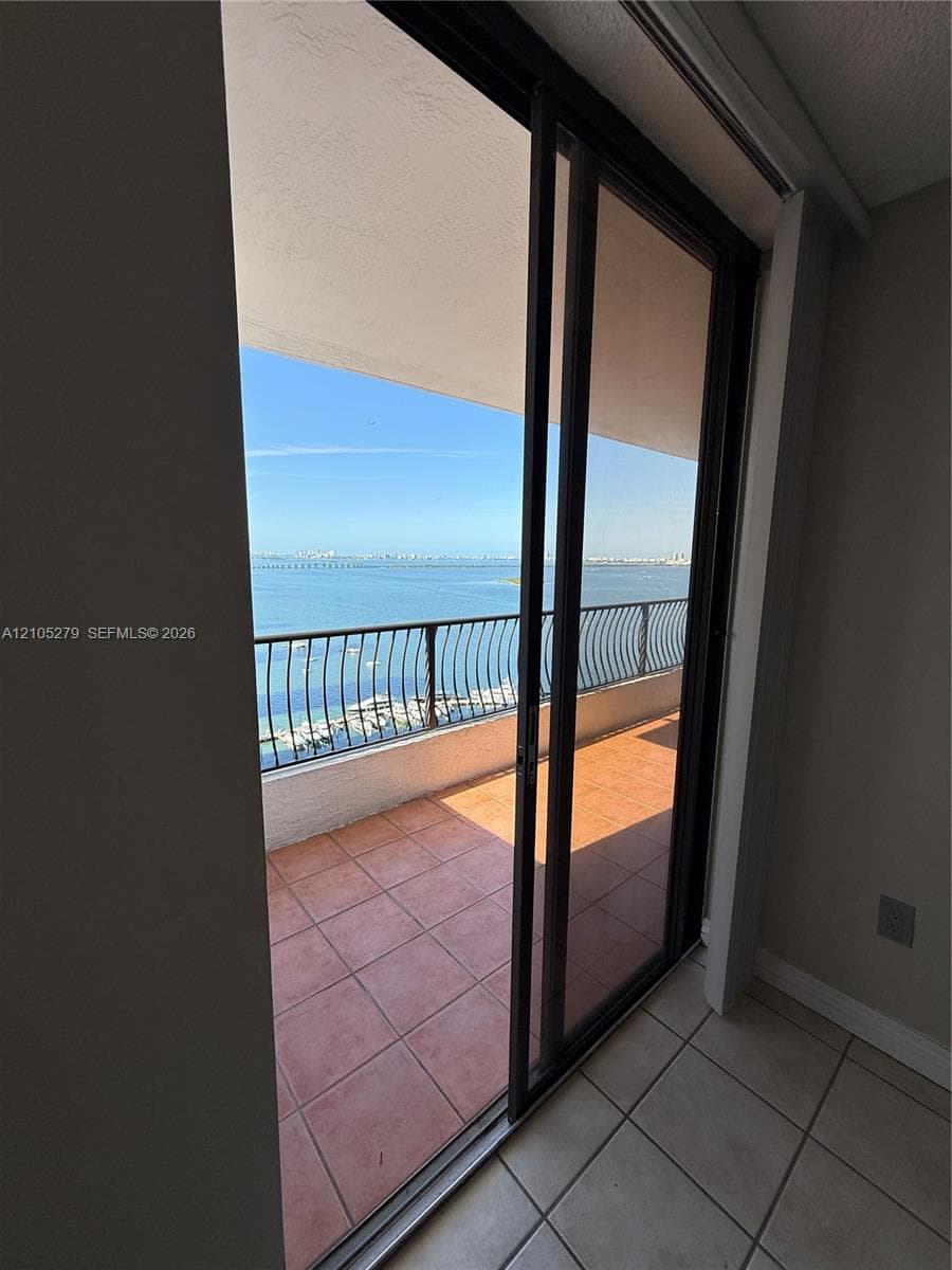 Sliding glass door leading to a balcony with terracotta tile flooring and a black metal railing