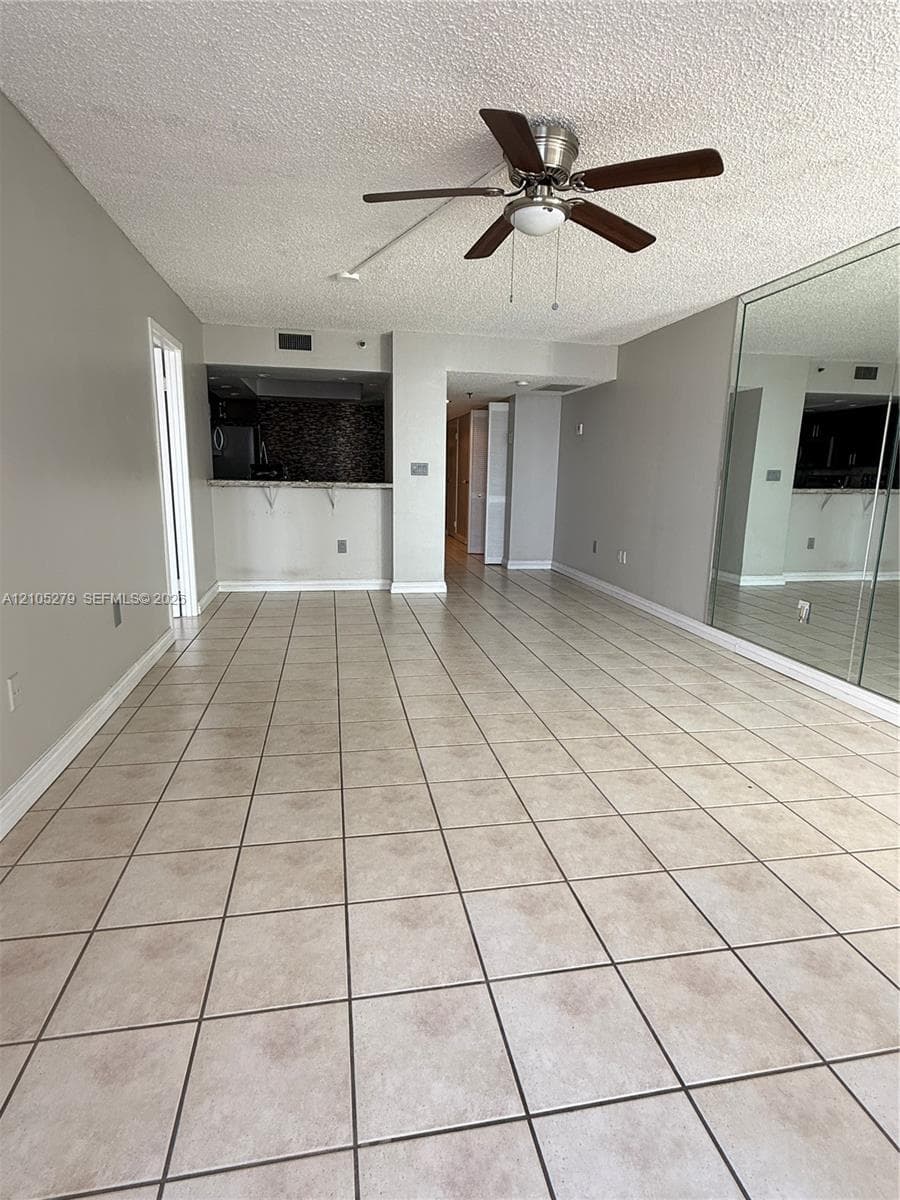 Tiled flooring throughout, featuring a ceiling fan with integrated lighting, mirrored wall panels, and a kitchen pass-through with a tiled backsplash