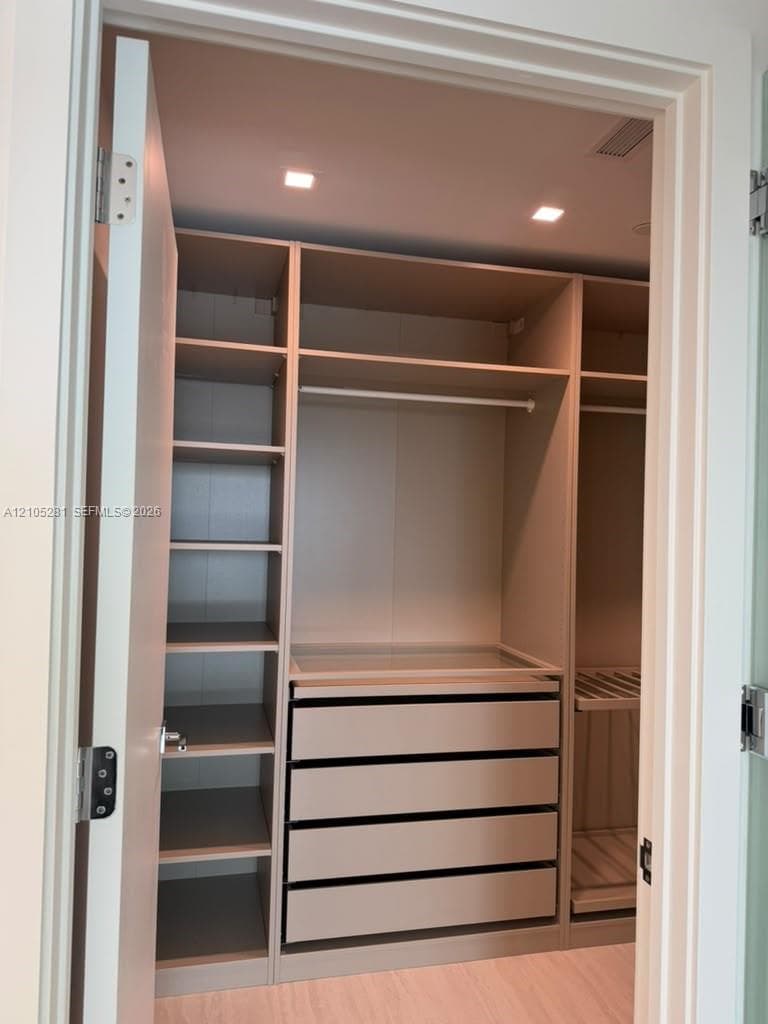 Custom walk-in closet featuring floor-to-ceiling built-in cabinetry, integrated shelving, four stacked soft-close drawers with glass-top display, dual hanging rods, and recessed LED ceiling lighting