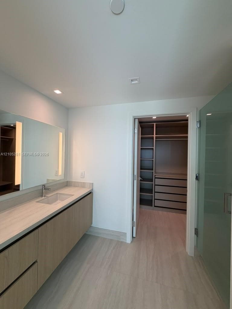 Floating vanity featuring a wood-finish cabinet, integrated countertop with rectangular basin, and recessed lighting