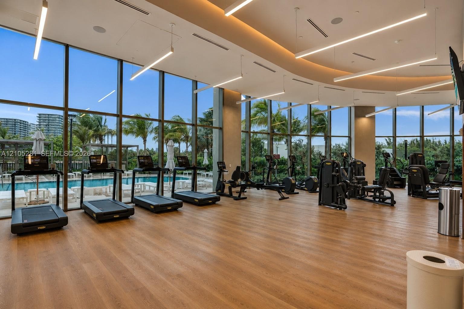 Fitness center featuring floor-to-ceiling windows, wood-finish flooring, recessed architectural lighting, and suspended linear light fixtures