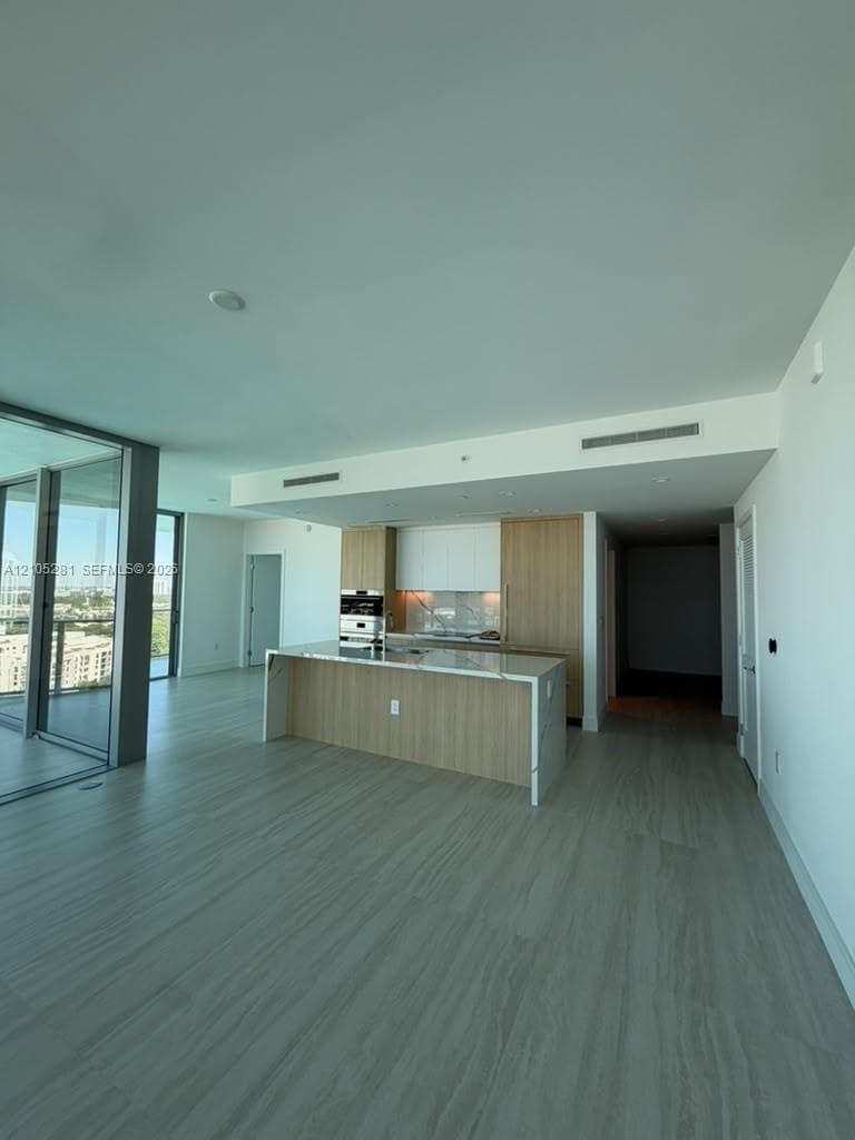 Kitchen featuring custom wood-finish cabinetry, a waterfall-edge stone countertop, built-in stainless steel oven, and expansive floor-to-ceiling glass sliding doors