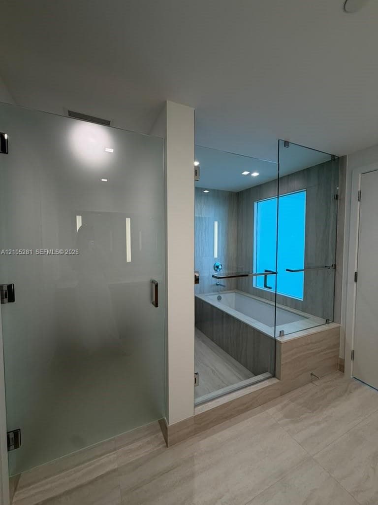 Frosted glass shower enclosure, deep soaking tub with a tiled surround, glass partition walls, and large-format tile flooring