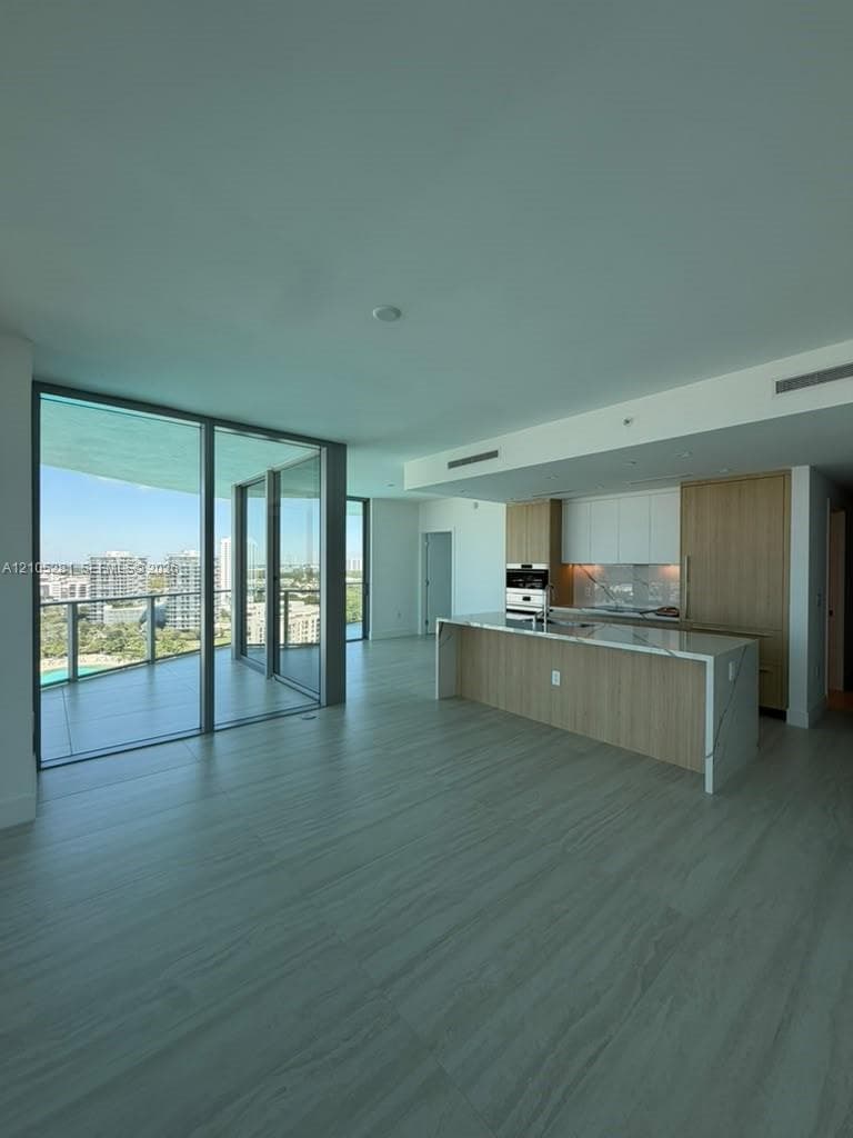 Open-concept kitchen featuring two-toned cabinetry, stone-surfaced waterfall island, and built-in appliances, accented by large floor-to-ceiling glass sliding doors leading to a private balcony