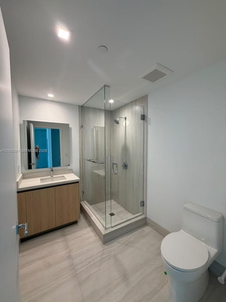 Bathroom featuring a wood-finish vanity with a rectangular undermount sink, a frameless glass-enclosed shower with floor-to-ceiling tile surround, and large-format neutral floor tile