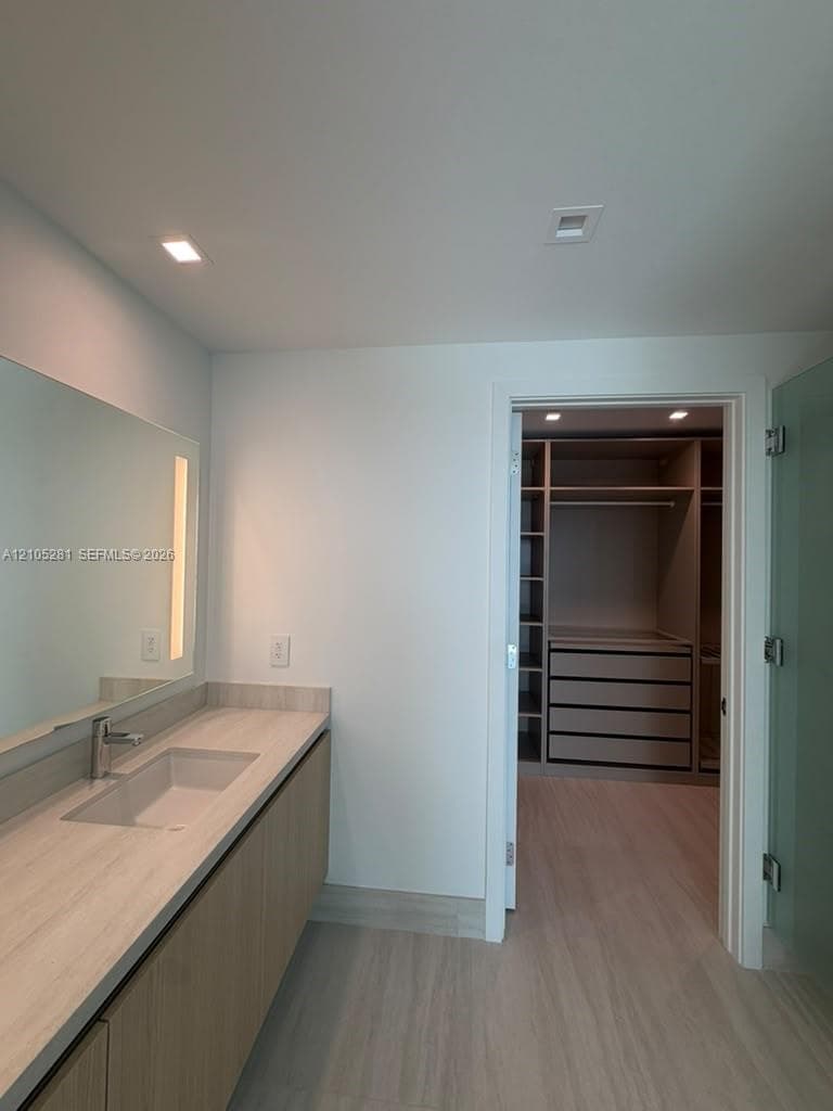 Floating vanity with a light-toned wood finish, integrated rectangular sink, wall-to-wall mirror, and walk-in closet featuring custom built-in shelving and drawers