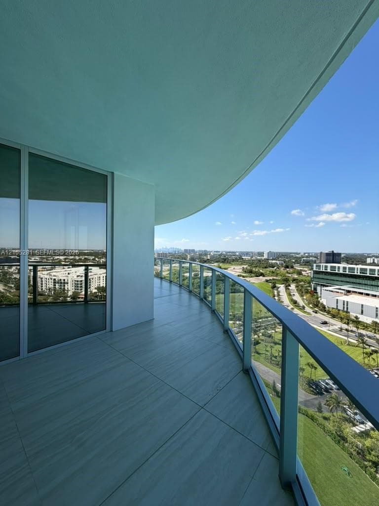 Curved exterior balcony featuring large-format tile flooring, a glass panel railing, and full-height sliding glass doors