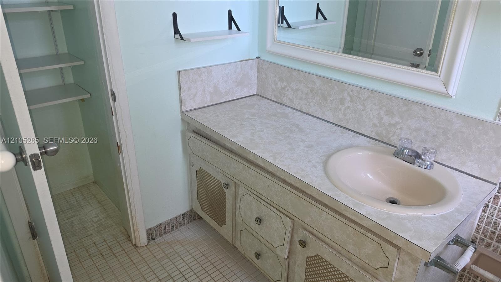 Vanity with stone-finish countertop, integrated oval sink, built-in storage cabinets, framed mirror, and built-in shelving