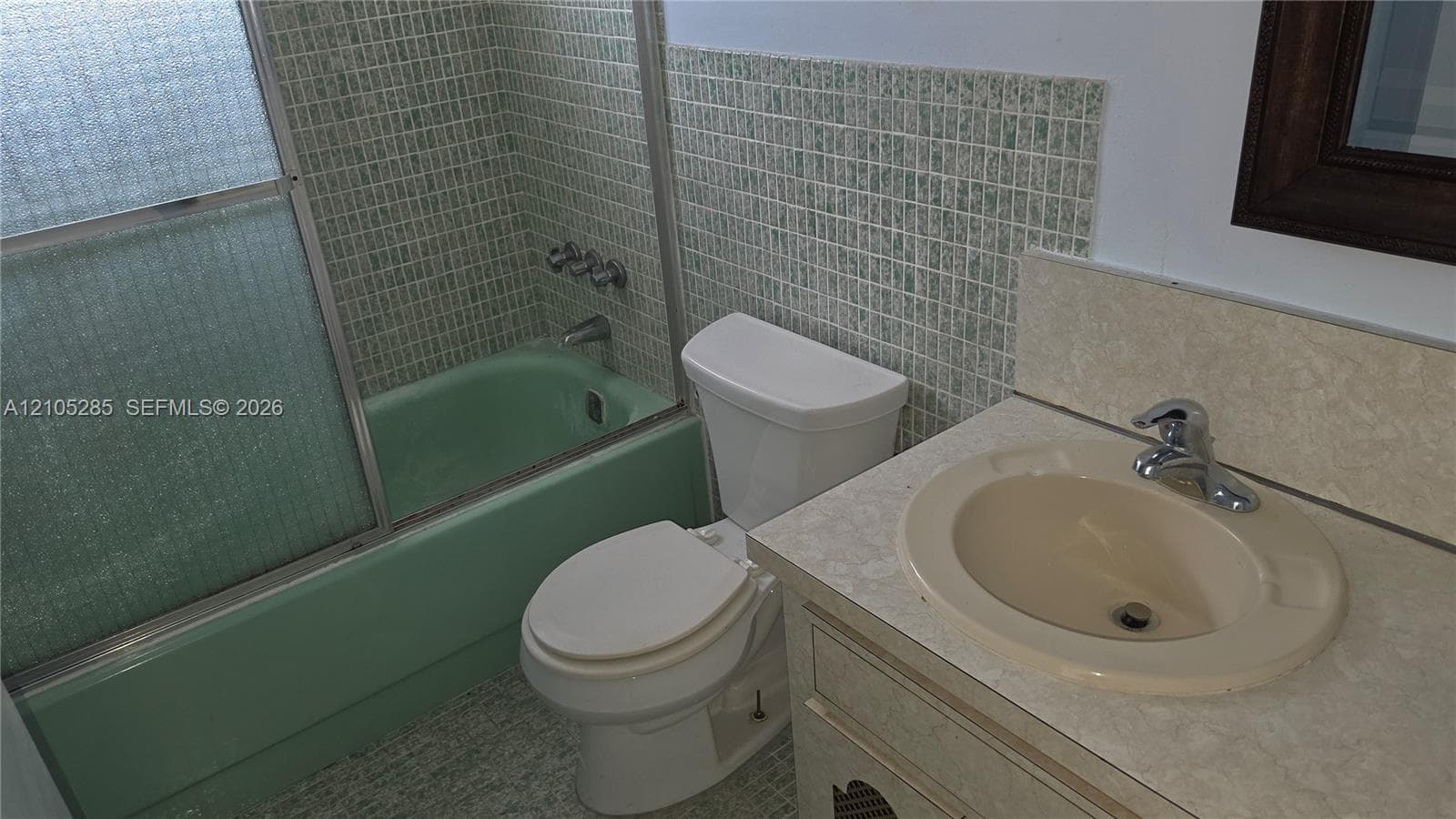 Bathroom featuring a recessed vanity with a neutral-tone countertop and integrated basin, bathtub with a sliding glass enclosure, and wall-mounted mosaic tile surround