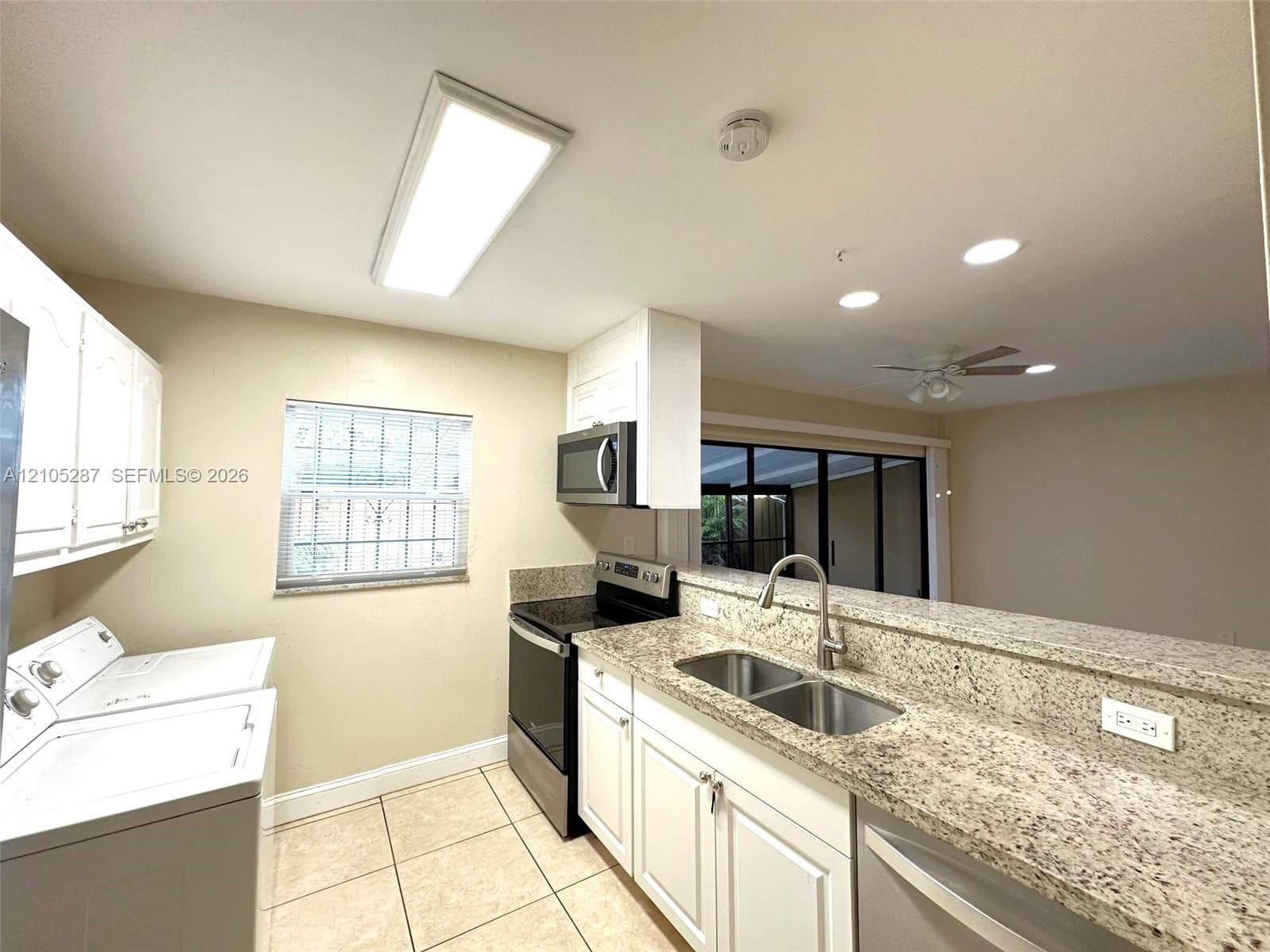 Kitchen featuring white cabinetry, granite countertops, stainless steel appliances, a double basin sink, and tile flooring