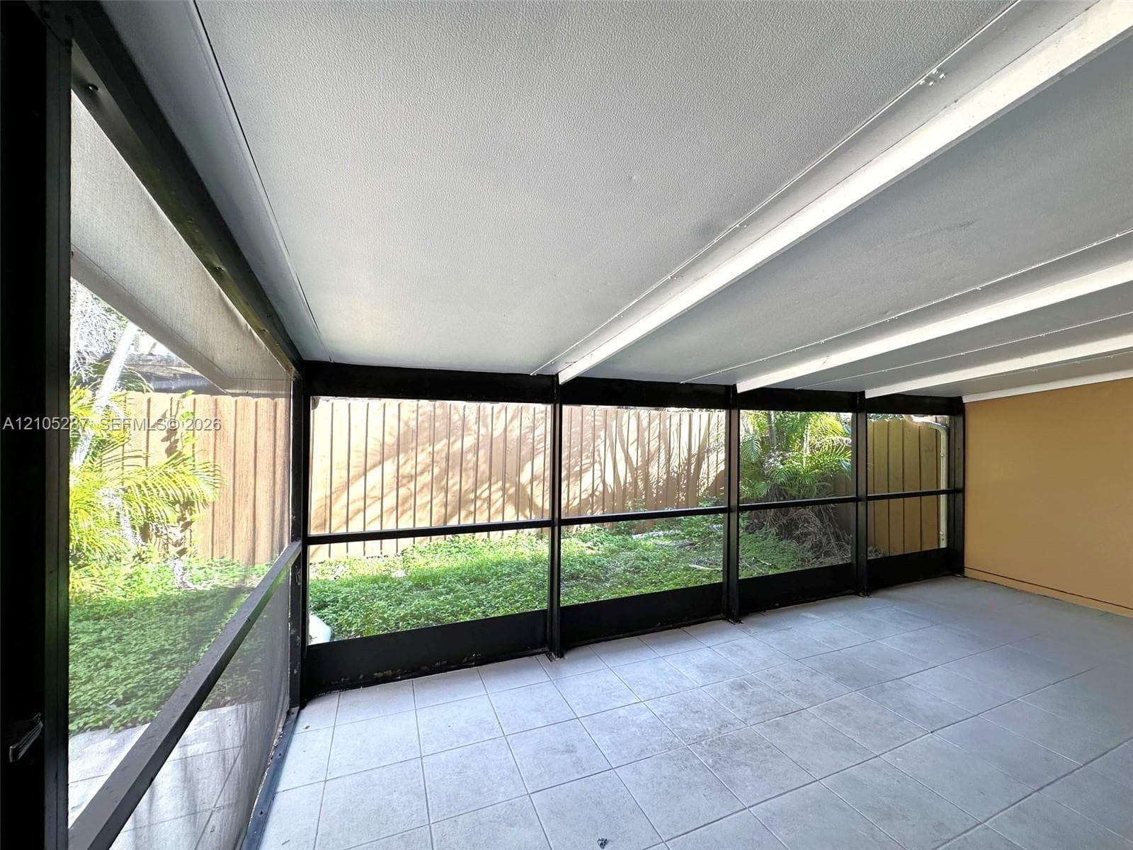 Screened-in patio featuring tiled flooring, a textured ceiling, and a solid perimeter fence