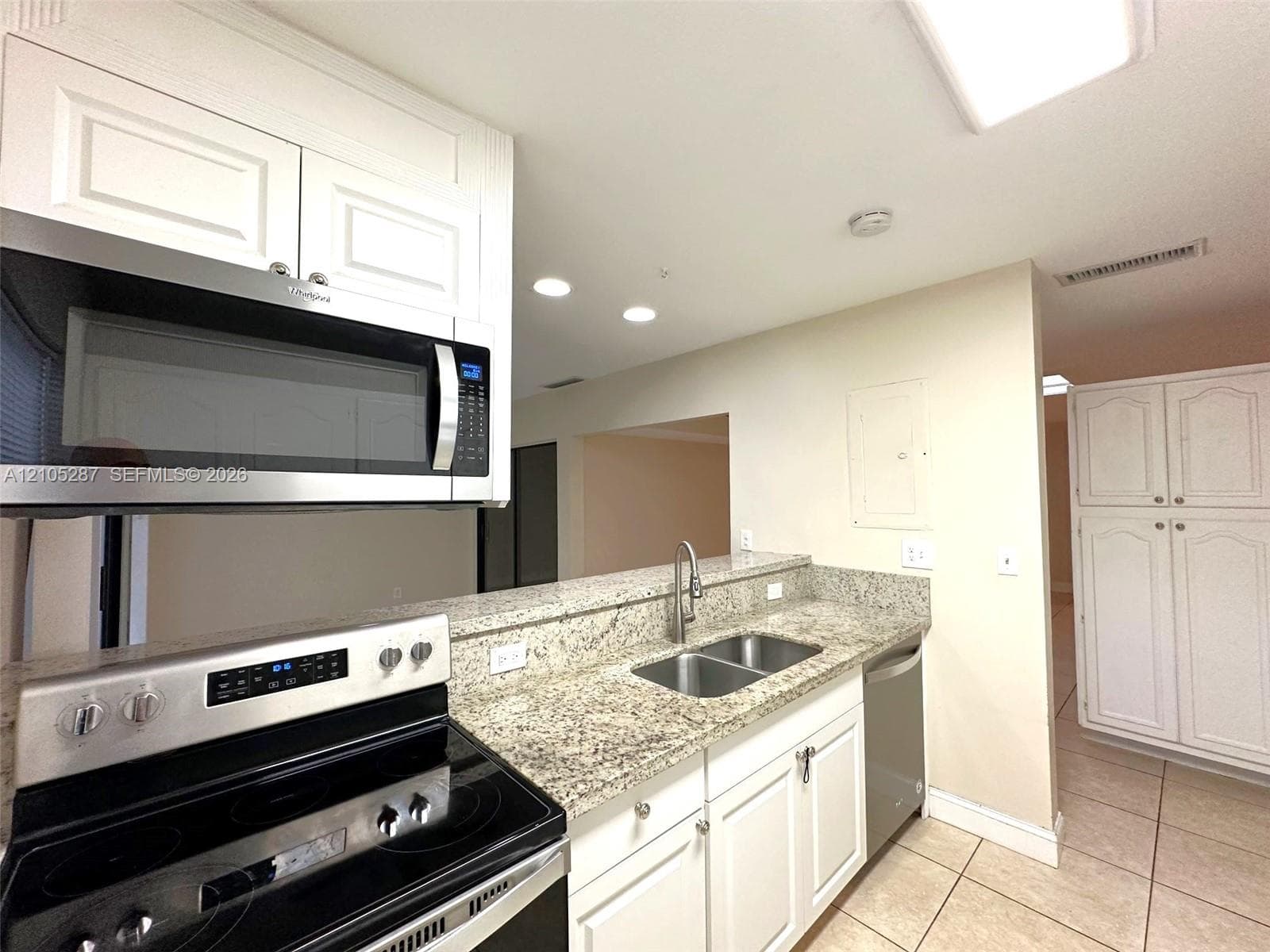 Kitchen featuring white cabinetry, granite countertops, stainless steel appliances, a dual basin sink with a high-arch faucet, and tile flooring