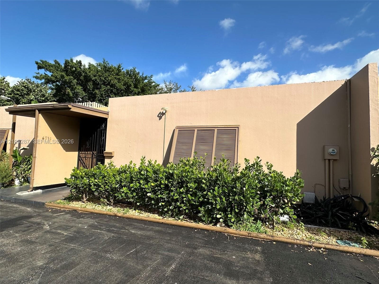 Stucco exterior with an attached awning, security gate, and mature perimeter landscaping