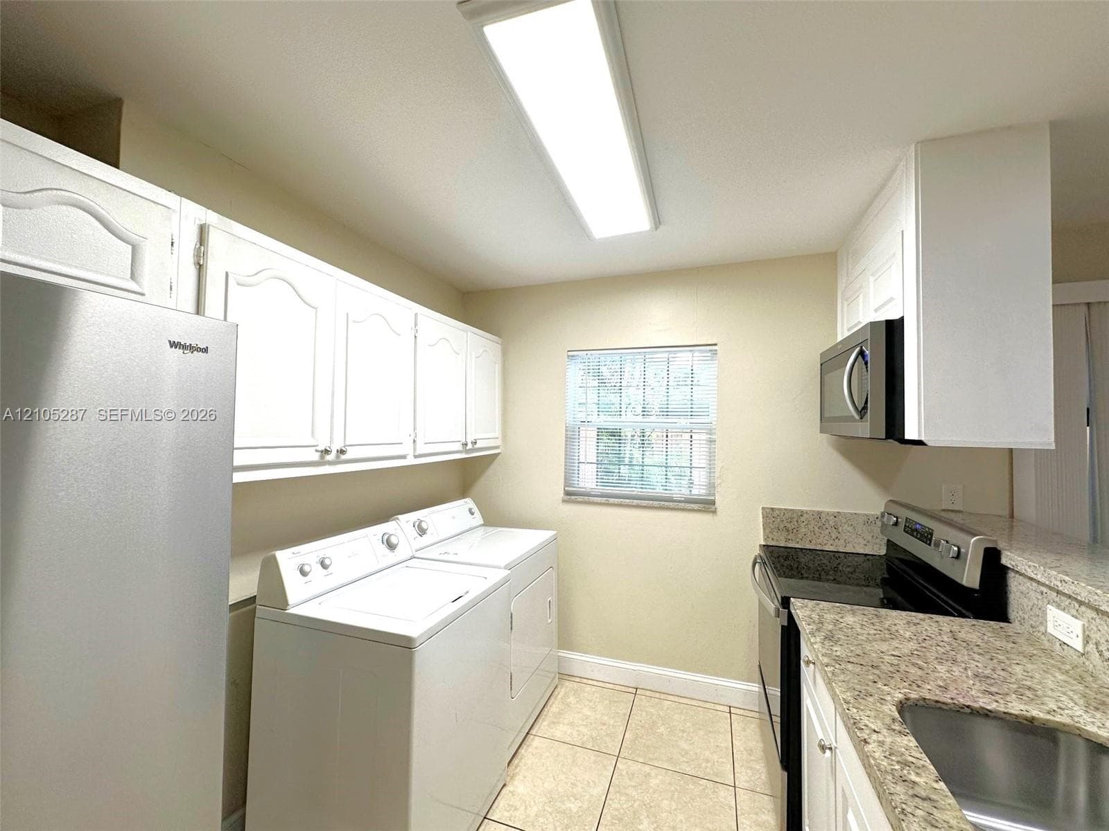 White cabinetry, tile flooring, stone-finish countertops, stainless steel sink, and a window with blinds